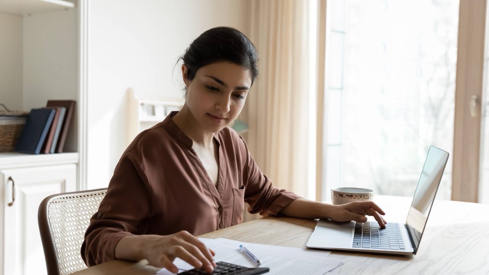 Woman going through her bills with a calculator and laptop