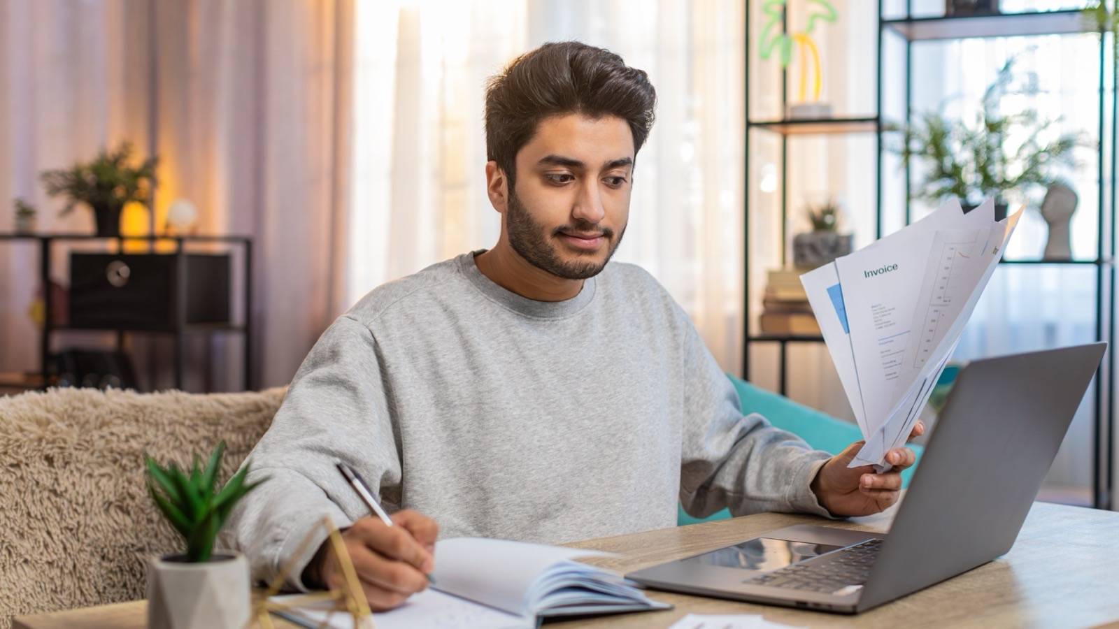 Man reviewing printed reports and taking notes beside a laptop