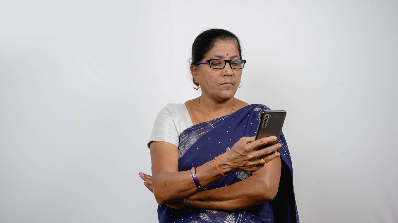 Woman in a sari and glasses looking carefully at her phone